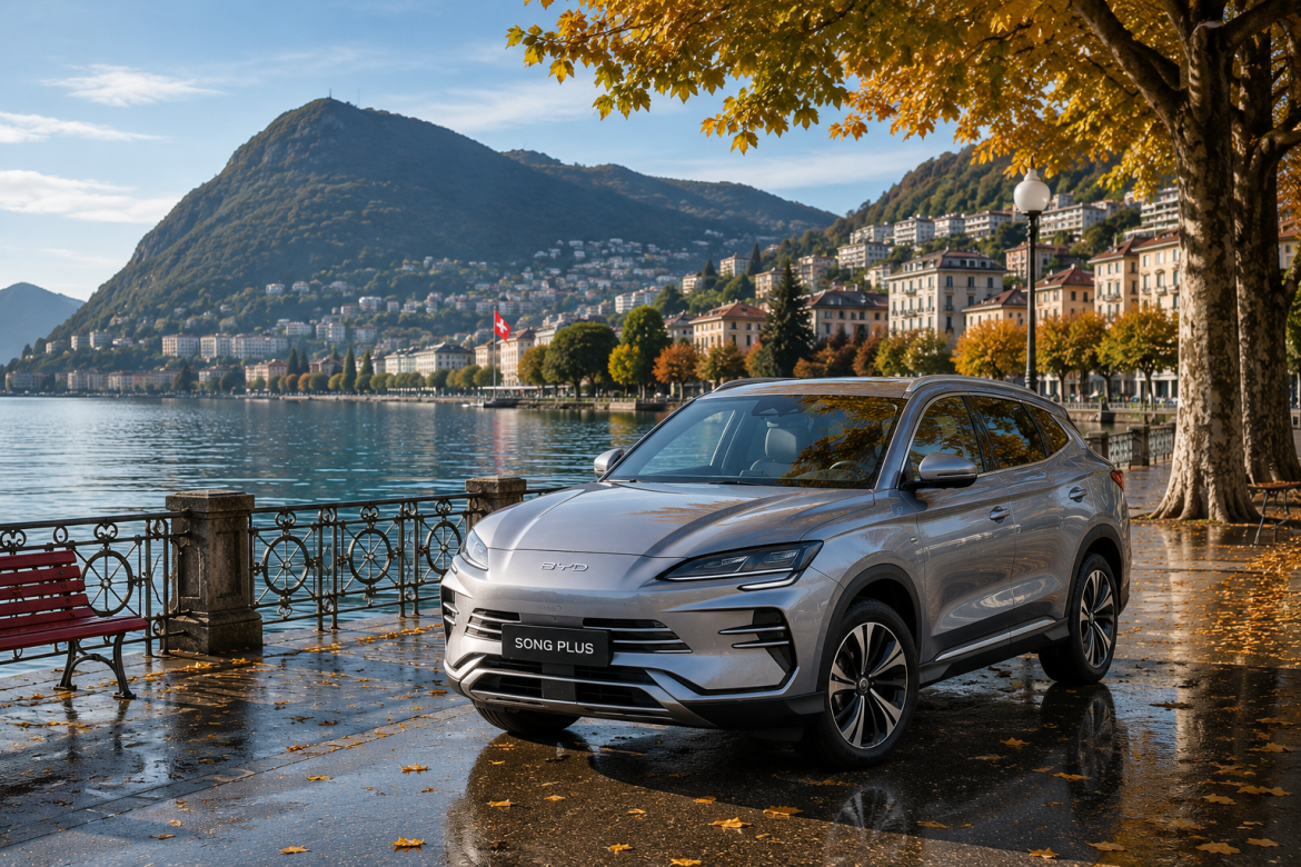 Сріблястий кросовер BYD Song Plus припаркований на мокрій набережній біля гірського озера з осінніми деревами та европейськими будівлями на задньому плані